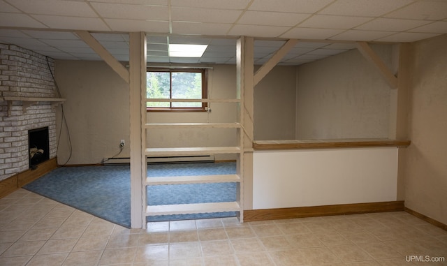 basement featuring a fireplace, light tile patterned floors, a baseboard heating unit, and a paneled ceiling