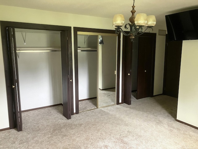 unfurnished bedroom featuring a chandelier, light carpet, and two closets