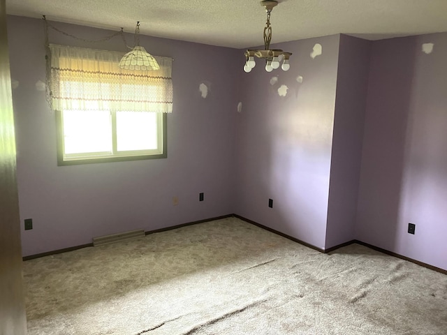 empty room with a textured ceiling, light colored carpet, and an inviting chandelier