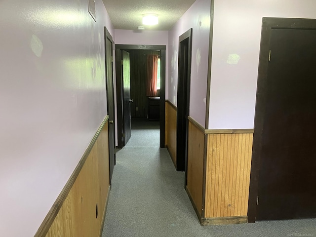 corridor featuring light carpet, a textured ceiling, and wooden walls