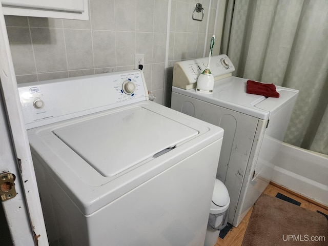 clothes washing area with washing machine and clothes dryer, tile walls, and wood-type flooring