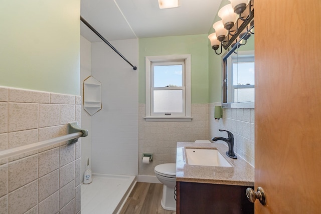 bathroom featuring toilet, tile walls, wood-type flooring, tiled shower, and vanity