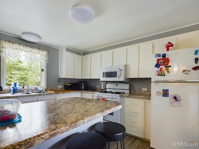 kitchen featuring dark hardwood / wood-style floors, light stone countertops, white appliances, a breakfast bar, and sink