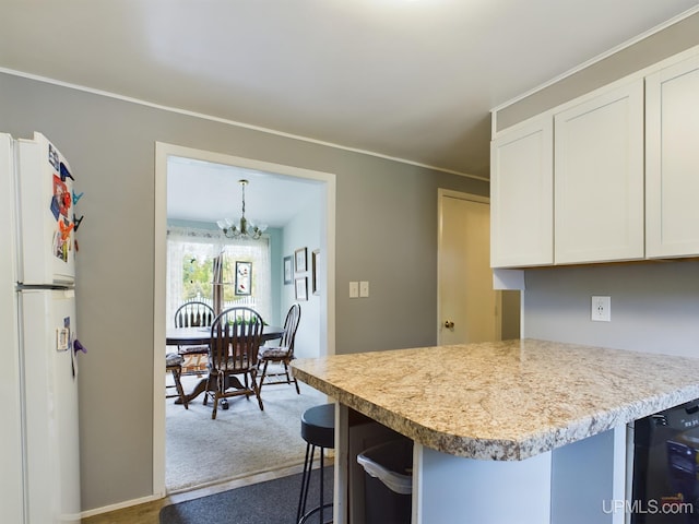 kitchen with white fridge, white cabinetry, a chandelier, a kitchen bar, and carpet