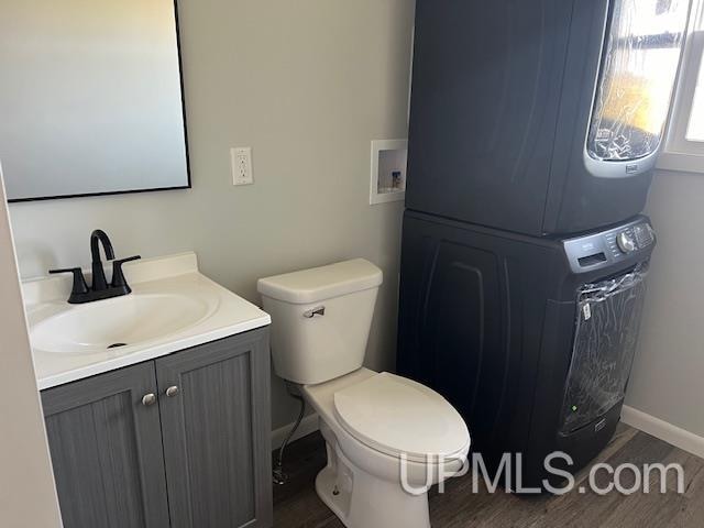 bathroom with hardwood / wood-style flooring, vanity, toilet, and stacked washing maching and dryer