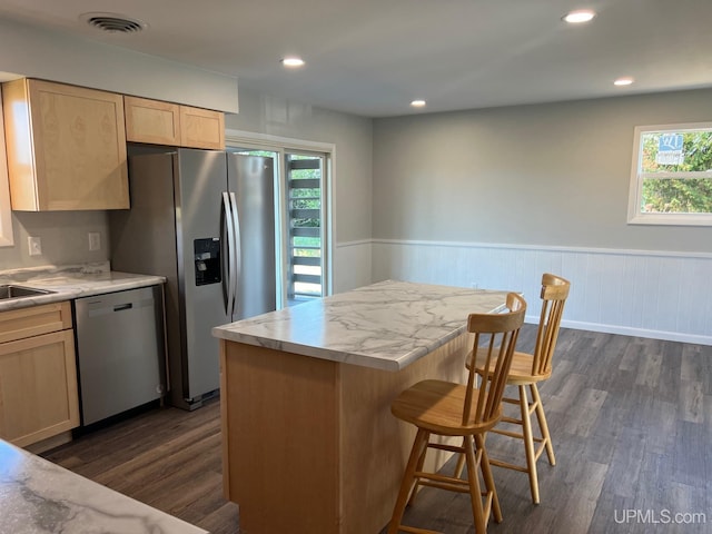 kitchen with light brown cabinetry, a kitchen island, dark wood-type flooring, and appliances with stainless steel finishes