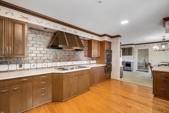 kitchen featuring pendant lighting, a notable chandelier, wall chimney range hood, and light hardwood / wood-style floors