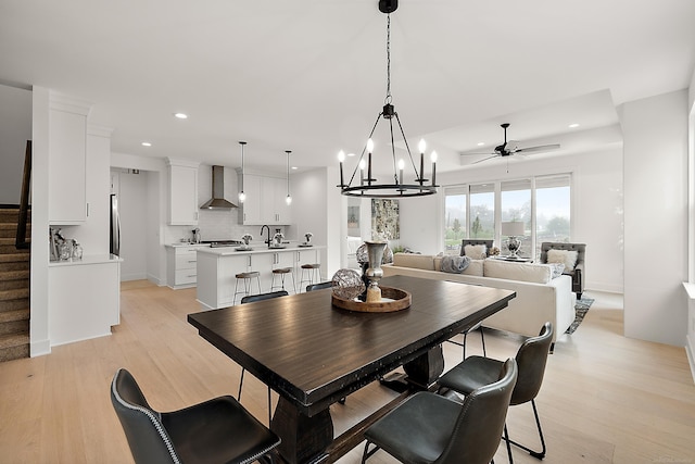 dining space featuring ceiling fan with notable chandelier, light hardwood / wood-style flooring, and sink