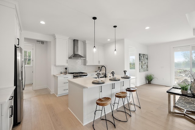 kitchen with a wealth of natural light, wall chimney range hood, white cabinetry, and a center island with sink