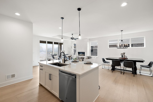 kitchen featuring a center island with sink, sink, white cabinetry, stainless steel dishwasher, and light hardwood / wood-style flooring