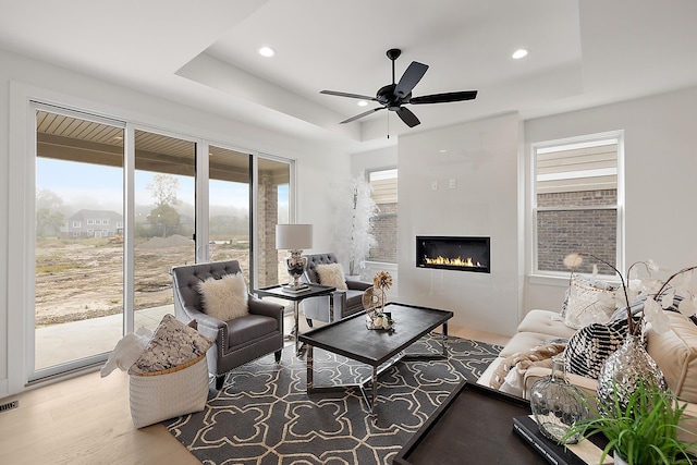 living room with wood-type flooring, ceiling fan, and a raised ceiling