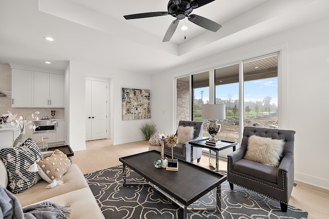 living room featuring light wood-type flooring, ceiling fan, and a tray ceiling