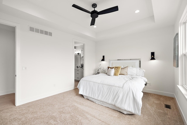 carpeted bedroom featuring ensuite bathroom, ceiling fan, and a tray ceiling