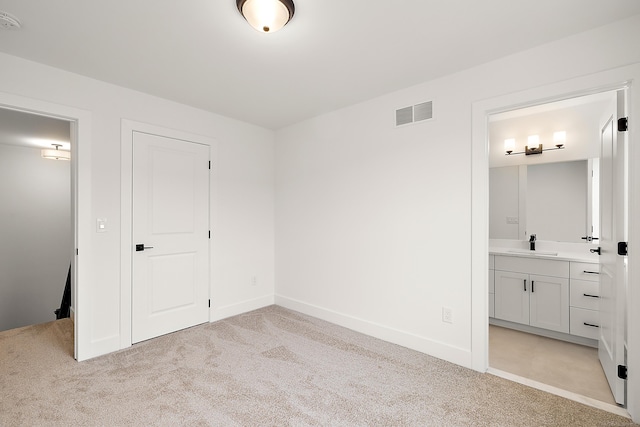 unfurnished bedroom with light colored carpet, ensuite bath, and sink