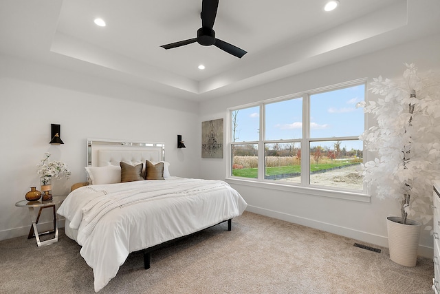 carpeted bedroom with ceiling fan and a tray ceiling