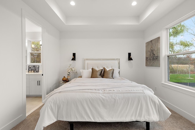 carpeted bedroom with a raised ceiling and ensuite bathroom