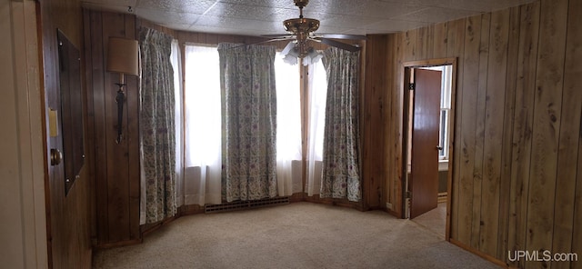 spare room featuring light carpet, ceiling fan, and wood walls