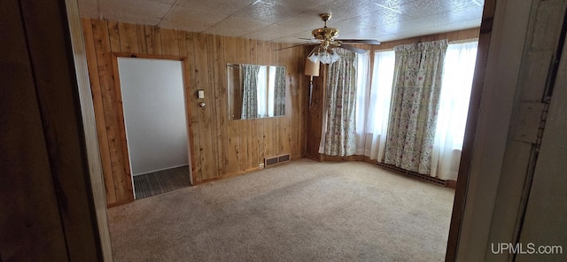 carpeted empty room with ceiling fan and wood walls