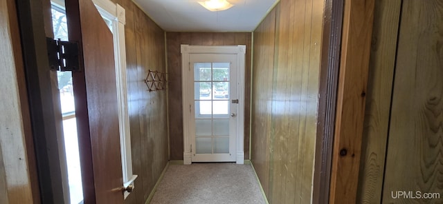 doorway to outside with light colored carpet and wooden walls