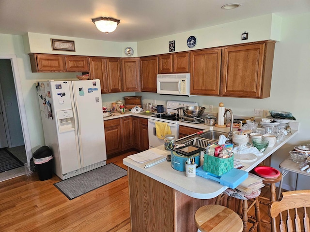 kitchen with a kitchen breakfast bar, white appliances, light hardwood / wood-style floors, kitchen peninsula, and sink