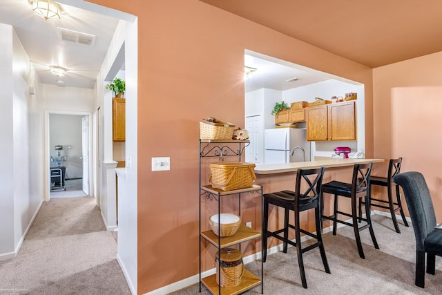 kitchen featuring light carpet, white refrigerator, kitchen peninsula, and a breakfast bar