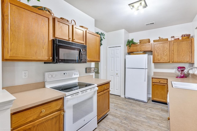 kitchen with light wood-type flooring, white appliances, and sink