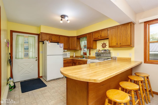 kitchen with white appliances, a kitchen breakfast bar, kitchen peninsula, and sink