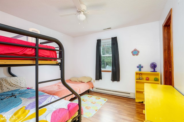 bedroom featuring hardwood / wood-style floors, ceiling fan, baseboard heating, and a textured ceiling