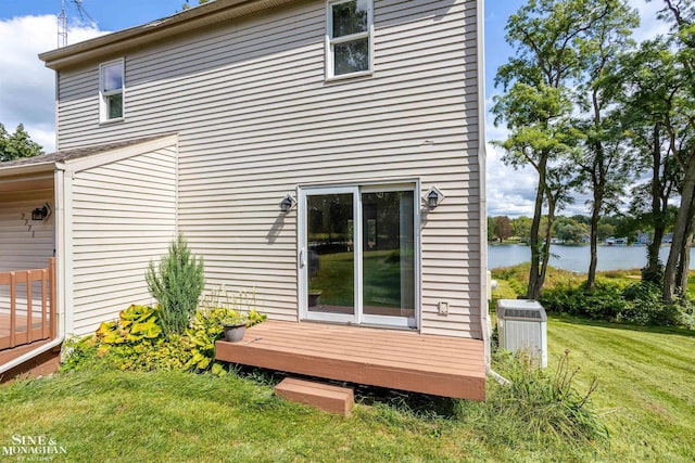 rear view of property featuring cooling unit, a lawn, and a deck with water view