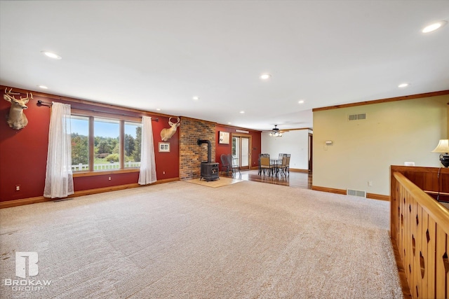 unfurnished living room with ornamental molding, ceiling fan, a wood stove, and carpet flooring