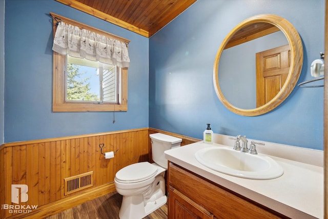 bathroom with wooden walls, wooden ceiling, hardwood / wood-style floors, toilet, and vanity