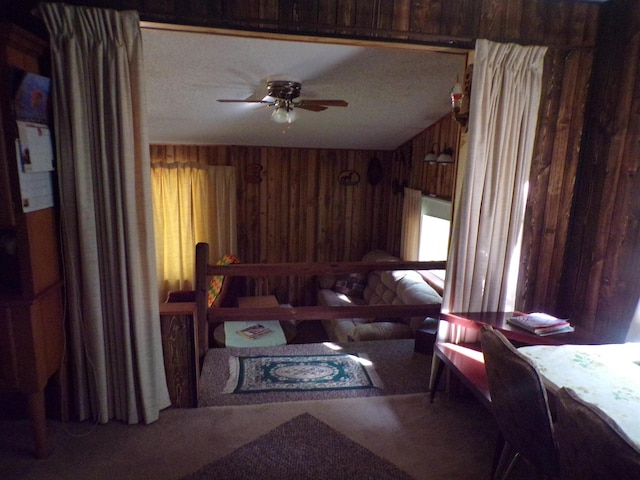 living room with a textured ceiling, ceiling fan, and wooden walls