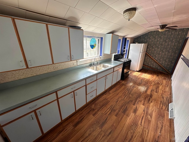 kitchen featuring black range with gas stovetop, vaulted ceiling, sink, white fridge, and white cabinetry