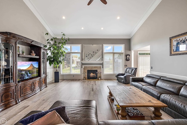 living room featuring crown molding, a high ceiling, ceiling fan, and light hardwood / wood-style flooring