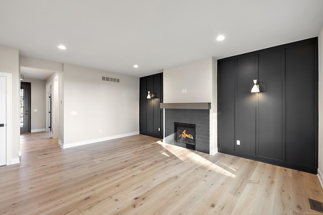 unfurnished living room with light wood-type flooring and a tiled fireplace