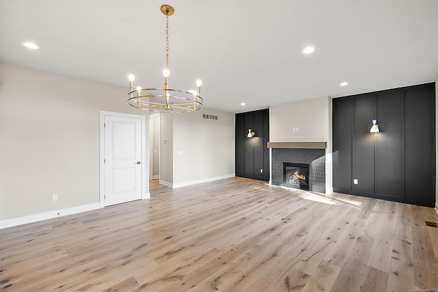 unfurnished living room with light wood-type flooring, a tiled fireplace, and a notable chandelier