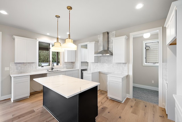 kitchen featuring white cabinets, sink, wall chimney exhaust hood, a center island, and light hardwood / wood-style floors