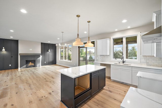 kitchen featuring light wood-type flooring, a tile fireplace, white cabinetry, and sink