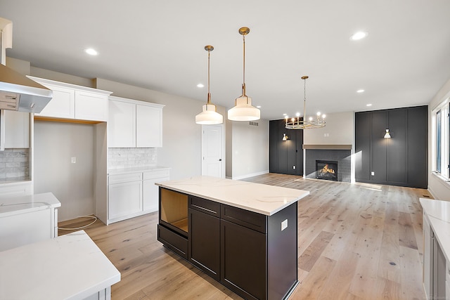 kitchen with light stone counters, white cabinets, hanging light fixtures, backsplash, and light wood-type flooring