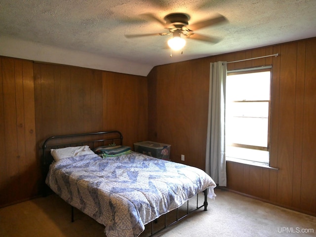 bedroom featuring ceiling fan, a textured ceiling, wood walls, and light carpet