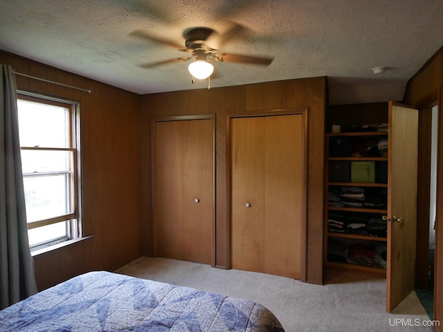 carpeted bedroom with ceiling fan, multiple closets, a textured ceiling, and wooden walls