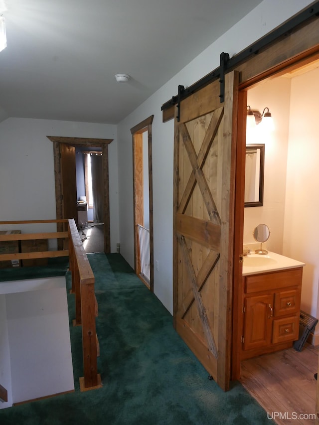 hall with dark carpet, vaulted ceiling, and a barn door