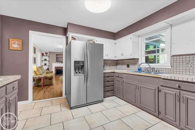 kitchen with stainless steel refrigerator with ice dispenser, a fireplace, gray cabinets, and white cabinets