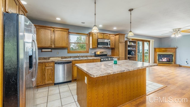 kitchen with a center island, brown cabinets, appliances with stainless steel finishes, a glass covered fireplace, and a sink