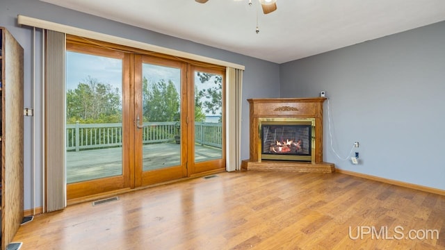 unfurnished living room with a ceiling fan, wood finished floors, visible vents, baseboards, and a glass covered fireplace