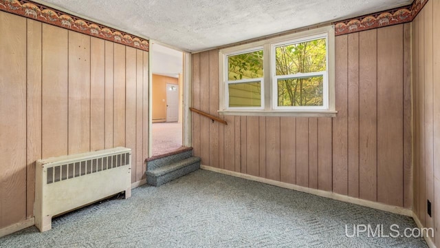 carpeted spare room with radiator, baseboards, wood walls, and a textured ceiling