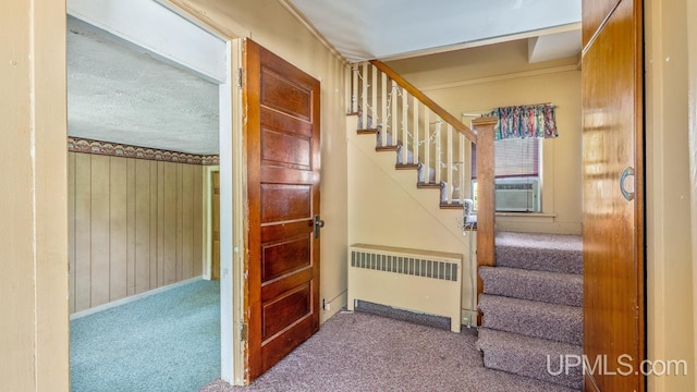 staircase with radiator, a textured ceiling, wooden walls, and carpet