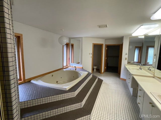 bathroom featuring a wealth of natural light, tile patterned flooring, vanity, and a relaxing tiled tub