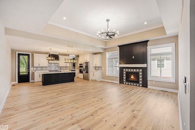 living room featuring ornamental molding, light wood-type flooring, a tray ceiling, and an inviting chandelier