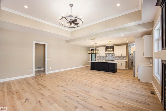 kitchen with white cabinetry, stainless steel refrigerator, pendant lighting, light hardwood / wood-style flooring, and a kitchen island with sink